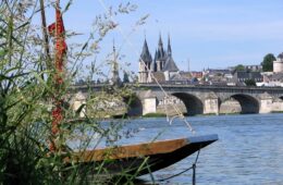 From one bank of River loire looking at part of boat and beyond stone bridge and towers of chateau rising on far bank