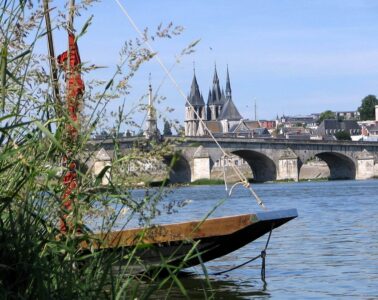 From one bank of River loire looking at part of boat and beyond stone bridge and towers of chateau rising on far bank