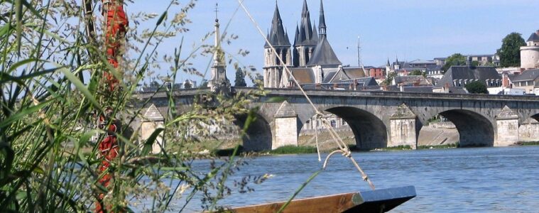 From one bank of River loire looking at part of boat and beyond stone bridge and towers of chateau rising on far bank