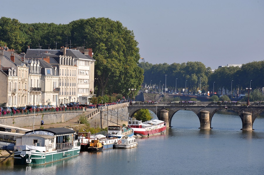 la Maine river at Angers view from river with boats tied up on quays with bridge over river and pale tall houses on left with big trees in leaf behind