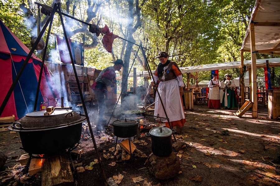 Camp with tents and people in costume at Renaissance festival in Le Puy with pot boiling on stove