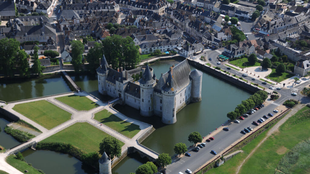 Aerial view of the Chateau de Sully from high up looking down onto river that washes its walls, and surrounding road and green park