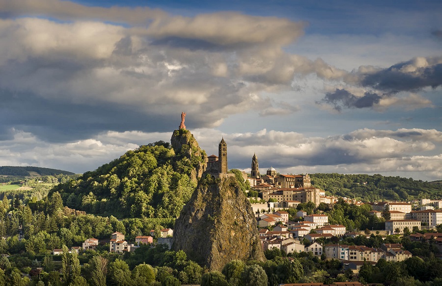 Le Puy-en-Velay dramatic photo with lowering clouds over the town showing pinacles of volcanic rock with monuments on top of chapel, cathedral and statue