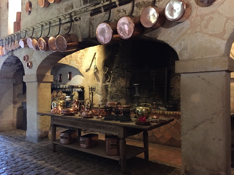Château de Brissac Loire Valley kitchen. With copper pots on walls, big fireplace in background and vaulted arches with table in middle