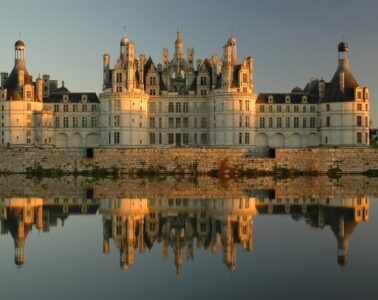 Chateau de Chambord across the water reflected. Huge beautiful stone chateau with lots of chimneys, towers, pinacles
