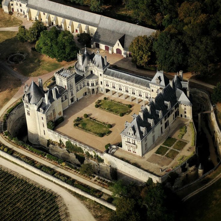 Château de Brézé in the Loire Valley aerial view from high up showing chateau white buildings on 3 sides of a large courtyard with flower beds and buildings stretching behing
