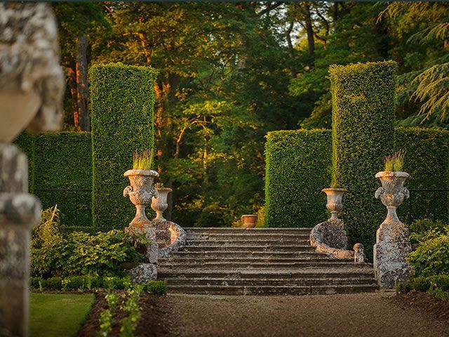 Chateau de Valmer gardens showing classical stone urns with plants on steps with yew trees made into rounds and green tree background
