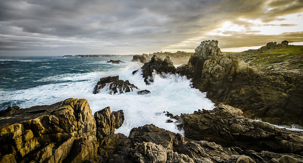 L'Ile de Ouessant Brittany island in autumn wind with waves on left crashing against rocks in semi circle and sea and grey clouds in background