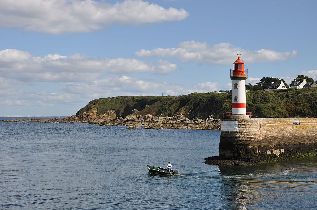 Port Tudy on Ile de Groix Brittany islands from port looking out with small boat beside jetty with small red and white lighthouse looking at headland sweeping round in background