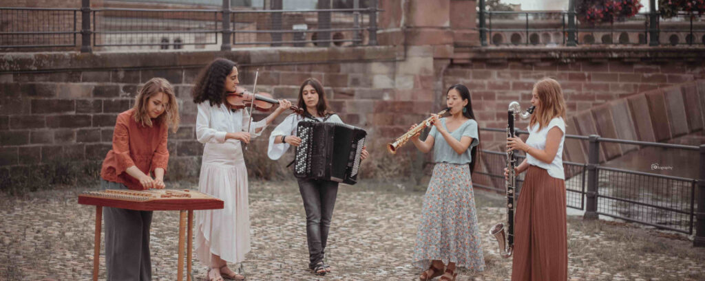 Strasbourg Musica group showing three women in outdoor space with different instruments