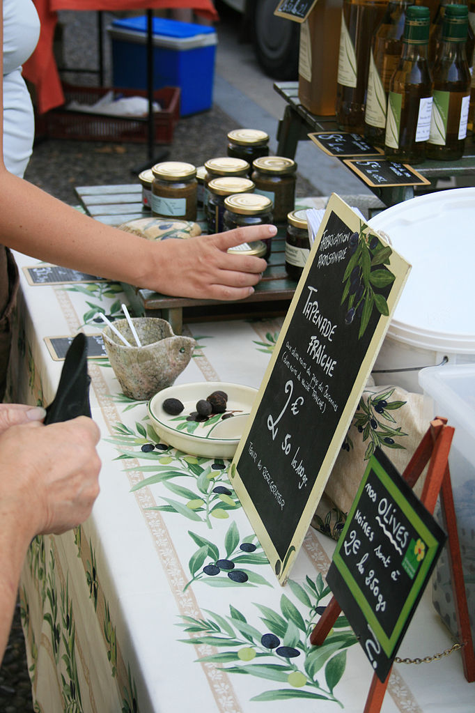 Vaison la romaine provence market with stall with tapenade, table cloth decorated with olives and tapenade jars with hand reaching out
