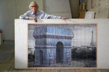 Christo standing behind a large picture of the Arc de Triomphe Wrapped