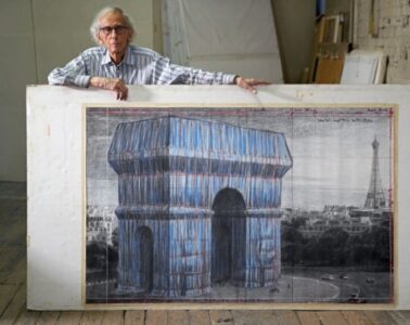 Christo standing behind a large picture of the Arc de Triomphe Wrapped