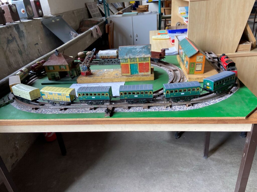 Model train with old fashioned train and green carriages on circular track with buildings behind