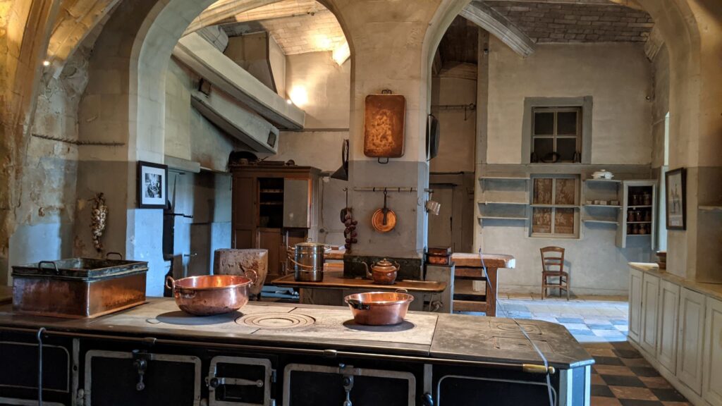 Château du Lude Loir Valley kitchens in huge vaulted room with range in middle with pots and pans, copper pans hanging on wall opposite
