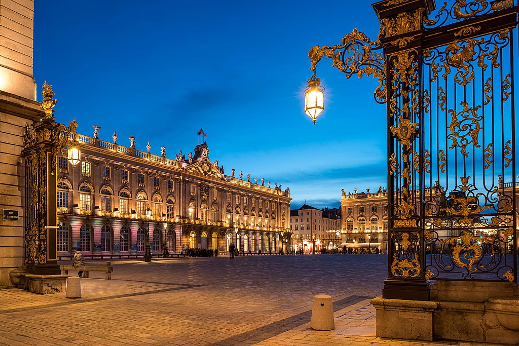 Place Stanislas in Nancy at night showing view through elaborate black and gold cast iron grill and long classical building bathed in spotlights