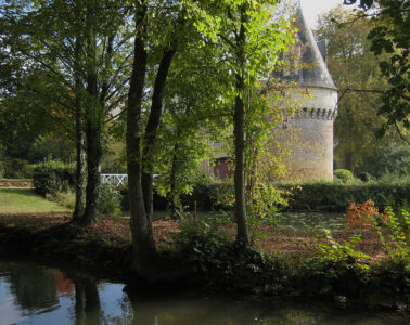 Chateau de Bazouges with trees and water in front partly shading a beautiful round stone tower with conical roof