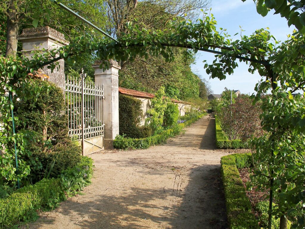 Château du Lude kitchen gardens showing wall with gate to one side, gravel path and beds to right