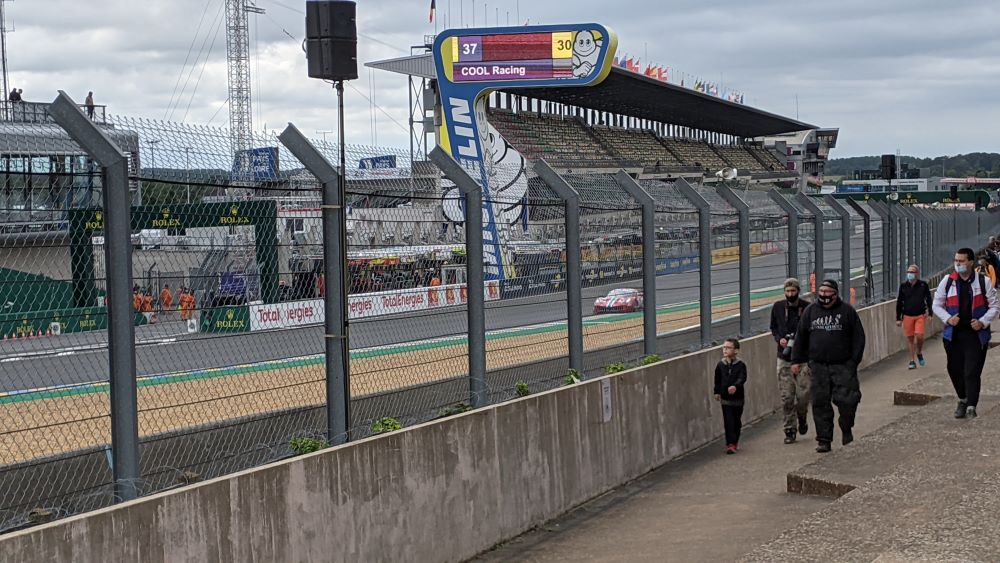 Looking through metal barrier at Le Mans race track with stands on other side
