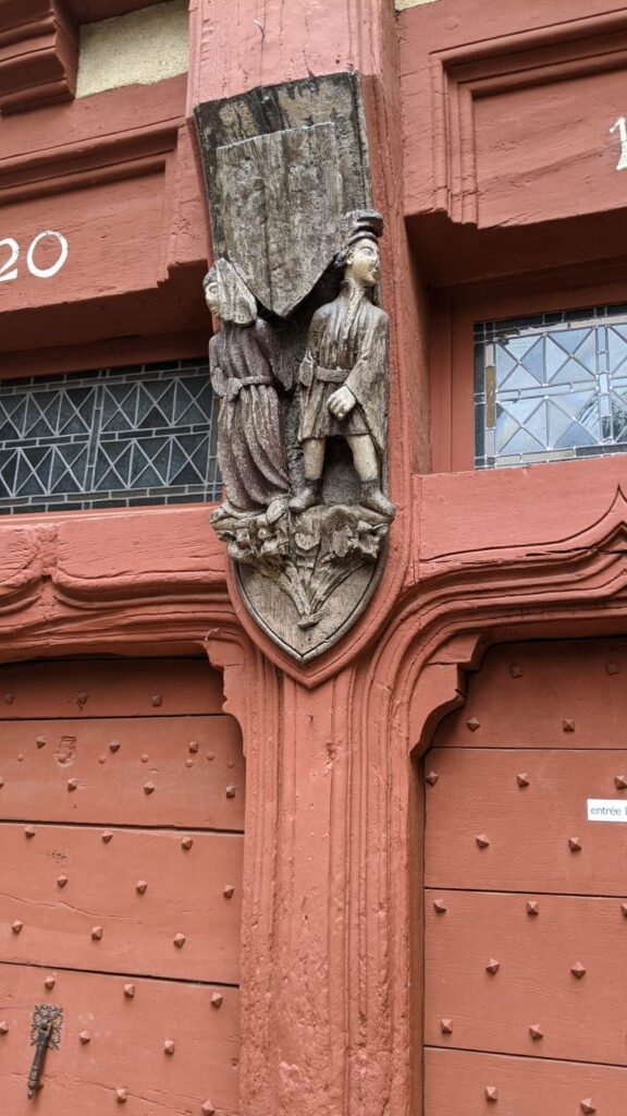 Two wooden figures on old house in Le Mans showing man peeing
