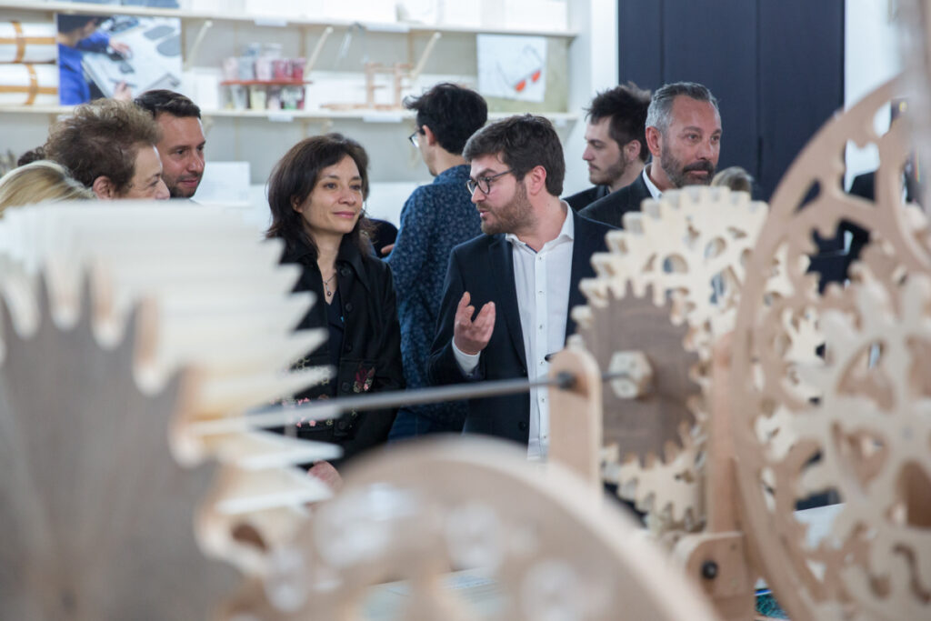 European Craft Days showing man and woman with others behind in front of what looks like white metal cogs and wheels of a giant clock