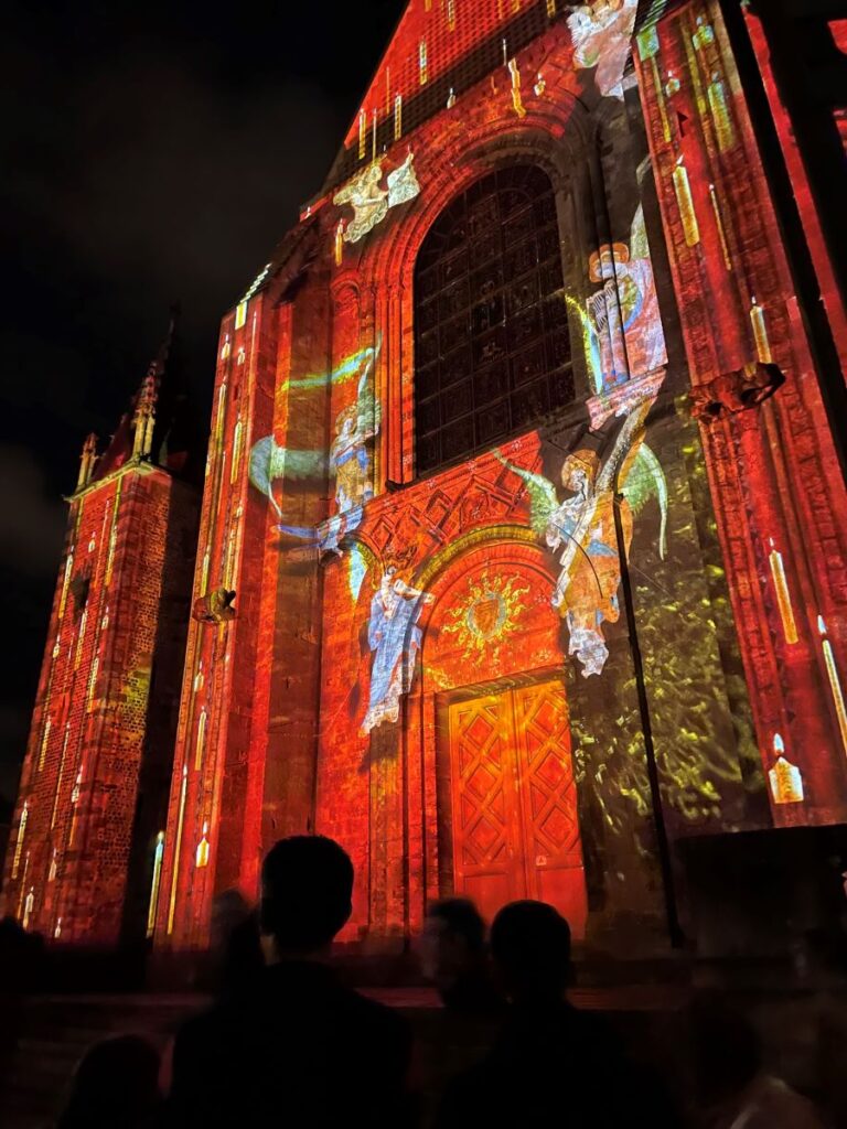 Le Mans cathedral lit up at front in red colour with blue and multi coloured angels climbing the front