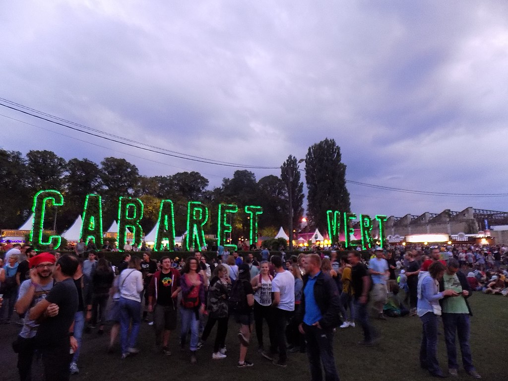 Le Cabaret Vertat night in Charleville-Meziers. Festival outside with green lit up sign Le Cabaret Vert i nfront of audience standing with dark sky behind