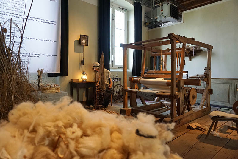 Parc de Wesserling eco museum showing pile of sheeps wool in front of old wooden loom in old room