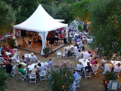 View from up above sideways of small marquee with no sides with jazz musicians at Ramatuelle with audience seated around stage