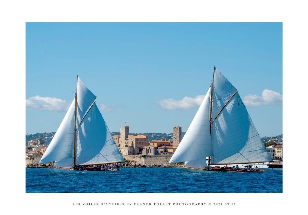 Les Voiles d'antibes event with two old yachts, sails at full stretch in blue sea in front of Antibe's castle and fort in background