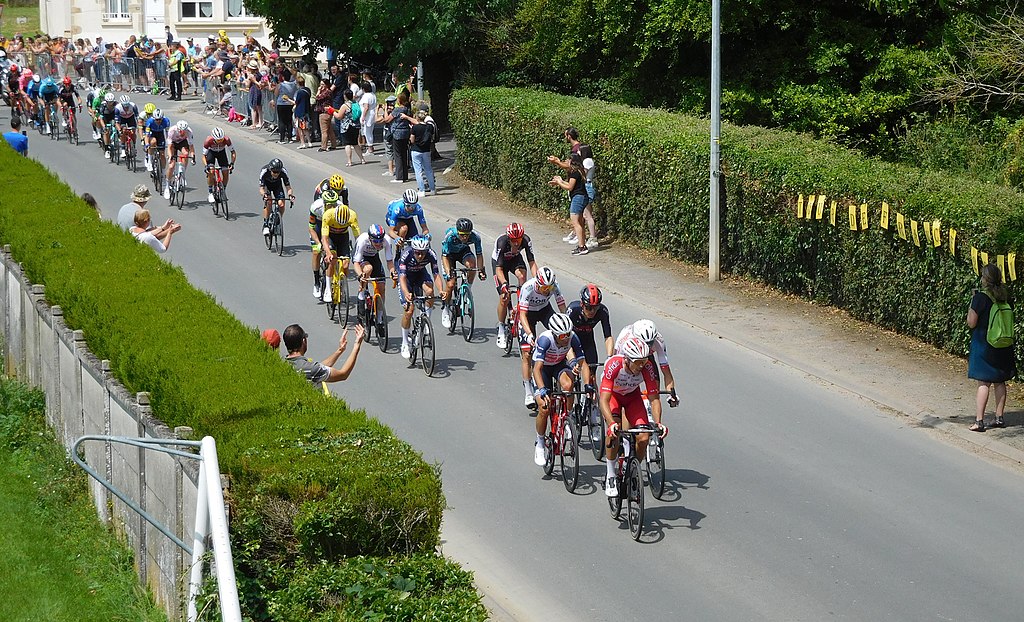 Baugy tour de France 2021 view from above with cyclists strung out along road in small town and a few spectators