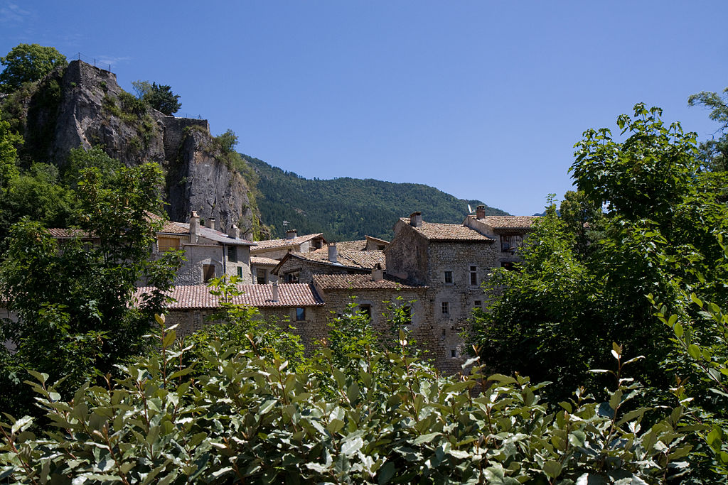 Chatillôn-en-Diois village perched very high on rocky mountain with higher rocks behind. Village of old stone houses, red tiled rooves and green in front