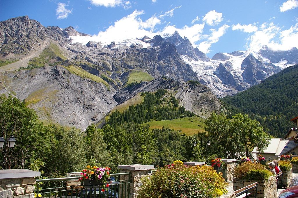 High mountains snow covered in background in summer, smaller hills and in front old stone houses in La Grave. La Meije mountain is main background image