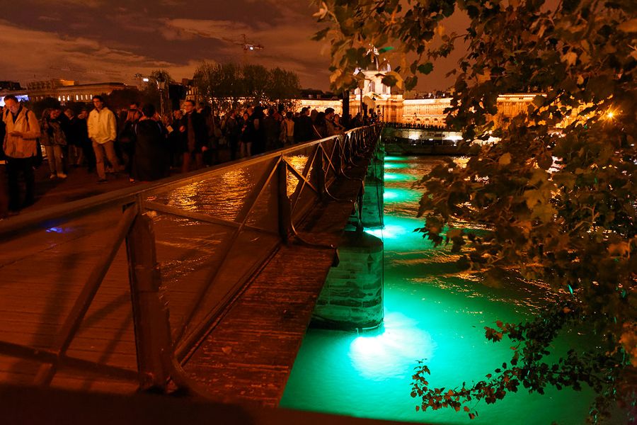 Nuit blanche in Paris with nighttime scene of canal litup andpeople on quays looking down at the turquoise water