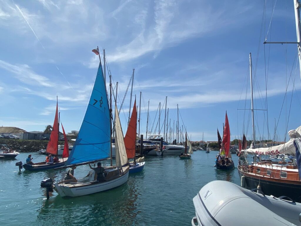 Little bots with different coloured blue , red and orange sails in the harbour following the Golden Globe