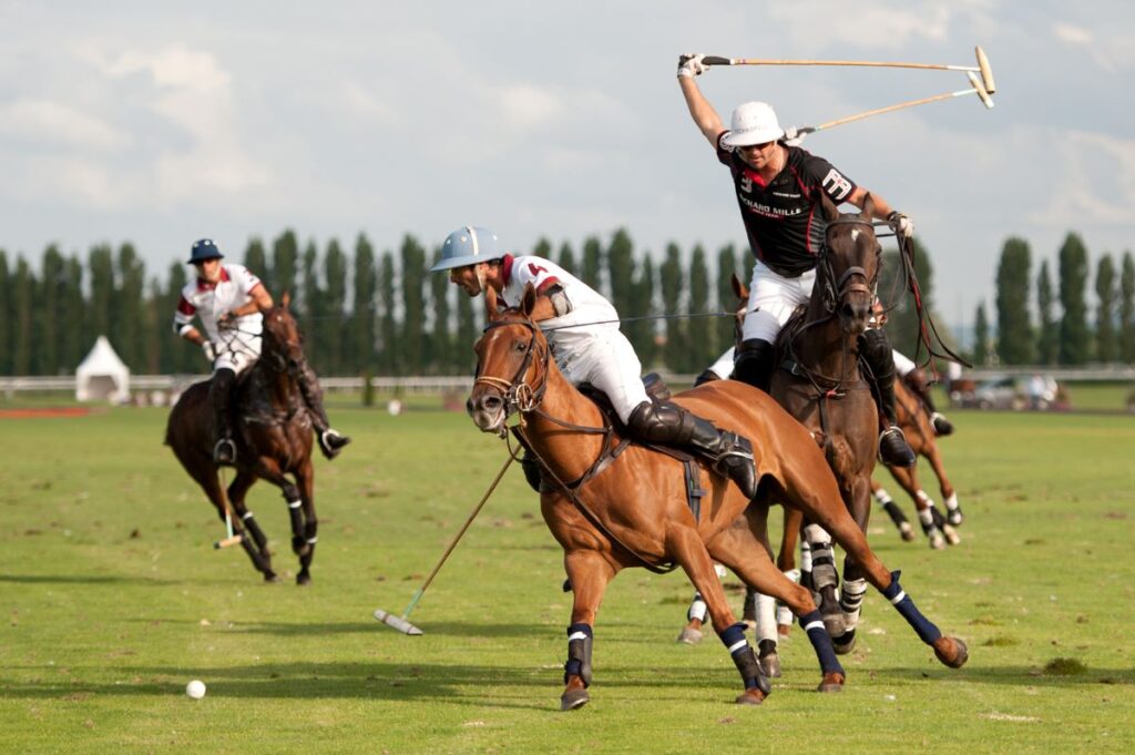 Polo match with three players, one with stick held high and one with stick near ground, all galloping