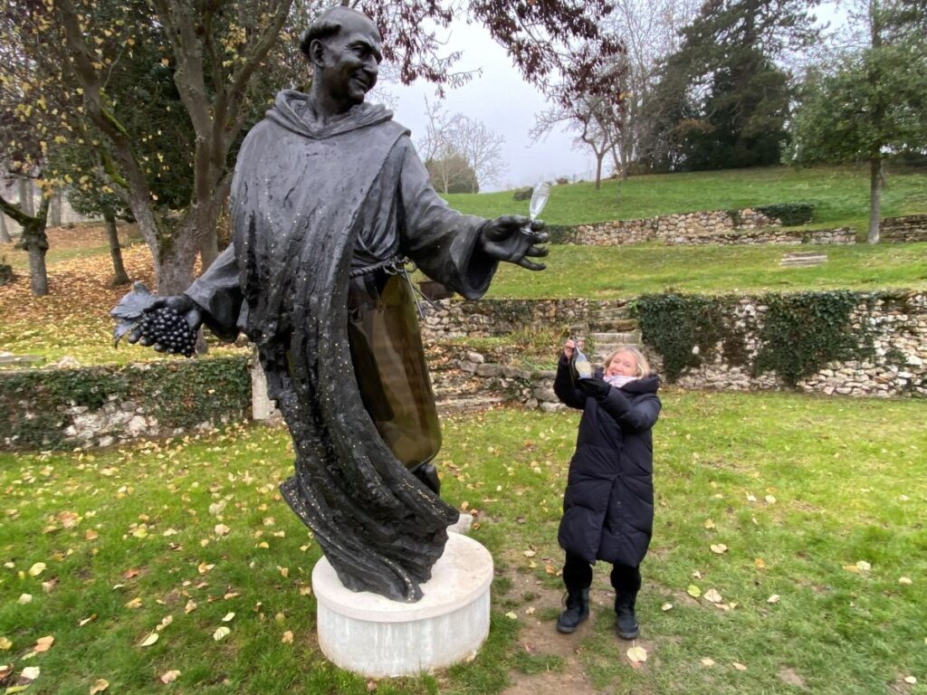Mary anne evans holding up glass of champagne beside large statue of dom perignon in Hautvillers