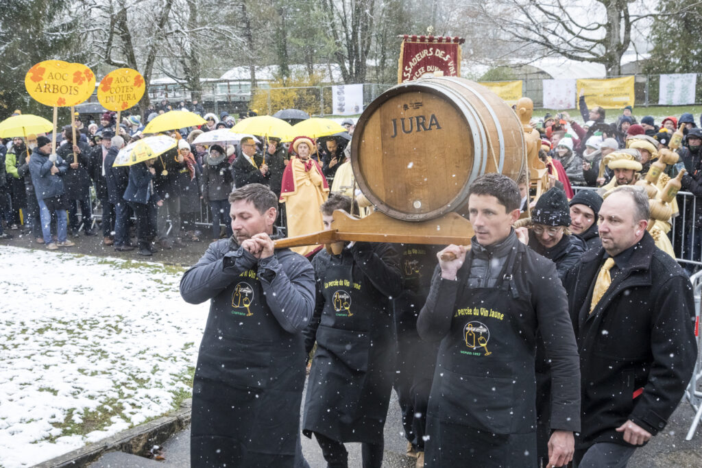 La Percee de jaunes Jura wine festival with 4 men carrying huge barrel of wine on shoulders walking through snowy streets