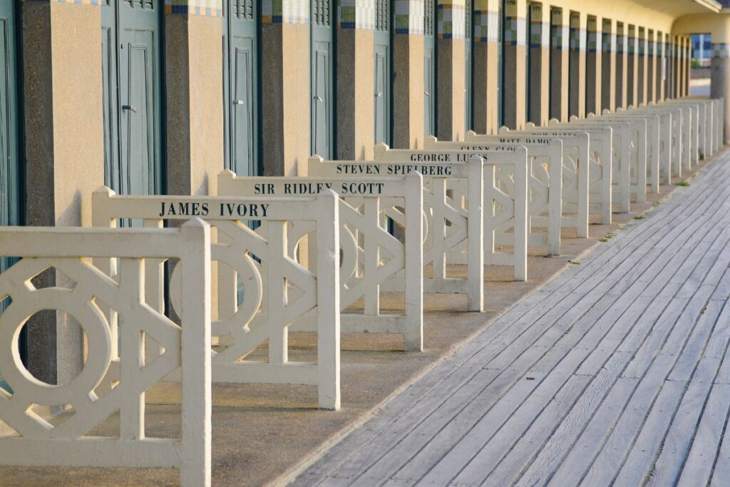 Beach huts at Deauville showing concrete abthing changing rooms with fences in front with names of Hollywood stars