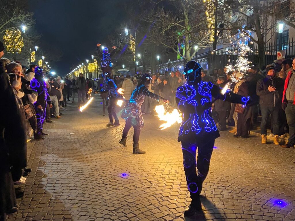 Les Habits de Lumiere procession showing weirdly dressed figures in blue and purples in street with spectators on both pavements