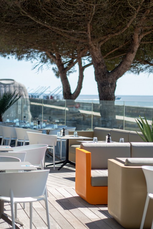 La Plage Bar and restaurant with terrace with tables, trees outside and blue sea beyond