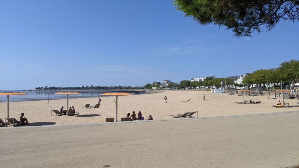 Saint-Nazaire beaches with long sandy beach with people on, ssea to left and trees and buildings in distance on right