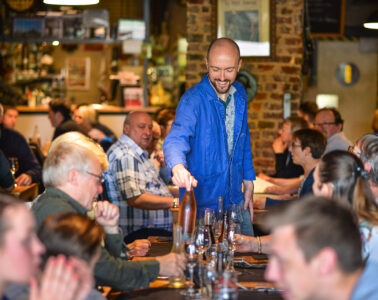 a l'fosse restaurant in northern France with waiter in blue smiling a he pours into glasses of whole table