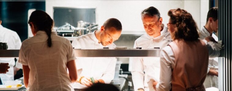 Le Cerisier open kitchen showing main chef looking on as young chef finishes a plate with waitresses waiting to pick it up