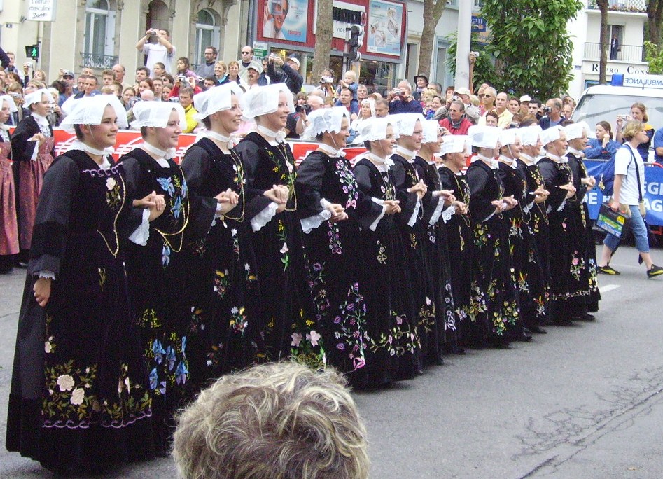 Interceltic Festival in Lorient, Brittany with line of women dressed in traditional breton costume of long black full skirted dreses and white bonnets marching in line down street