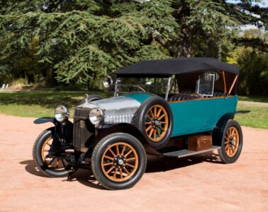 Henri Malartre car museum in Lyon. Large car parked outside with trees in background. Soft top; spare wheel on side, green painted