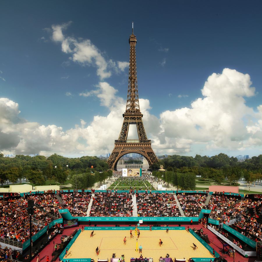 Image of Eiffel Tower Stadium for Paris Olympics 2024 with tower in background against blue sky and clouds, stands on both sides and sandy arena in front