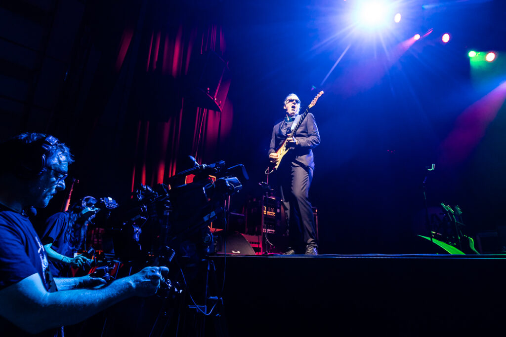 Joe Bonamassa on stage at Marciac jazz; mainly blue, him in suit with guitar