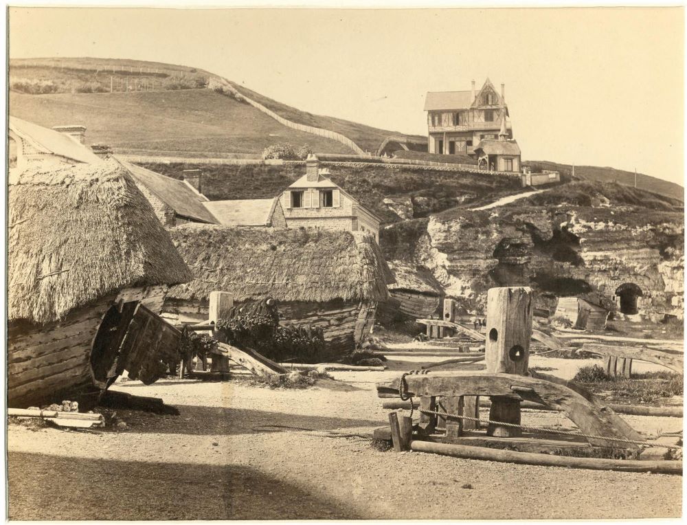 Sepia photograph by Alphonse Davanne of Etretat in 1862 showing hill in background, large house and empty cobbled streets