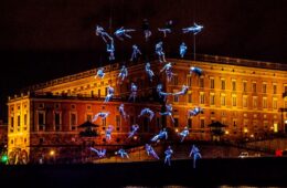 aquanauts show Caen Millennium with athletes suspended in mid air dressed in blue with building behind at night